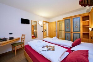 A hotel room with two beds, a desk with a chair, a TV, a mirror, and a wardrobe.