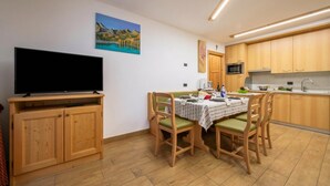 A dining area with a table set for four, wooden cabinets, a flat-screen TV, and a painting on the wall. - Tamigi (Livigno)