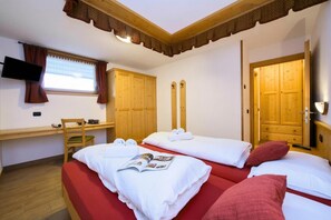 A room with two beds, a desk, a television, and wooden doors. - Tamigi (Livigno)