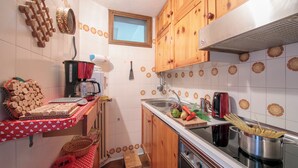 Une cuisine de taille réduite, dotée de meubles de rangement en bois, d’une cuisinière, d’un évier et de divers ustensiles de cuisine.