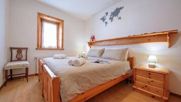 Uma cama de madeira com cabeceira, uma mesa de cabeceira com abajur e uma pequena cadeira de madeira.