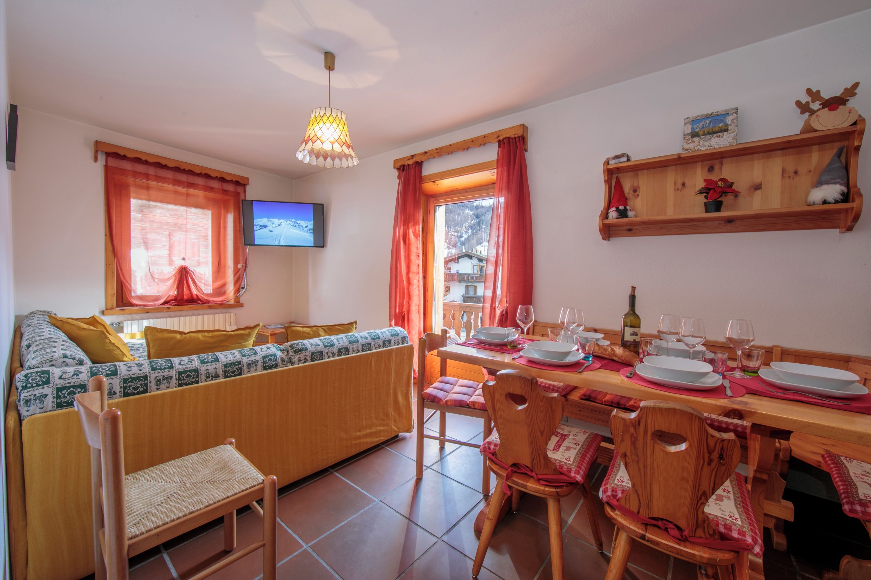 A cozy living room with a sofa, dining table, chairs, a TV, and a wooden shelf with decorations.