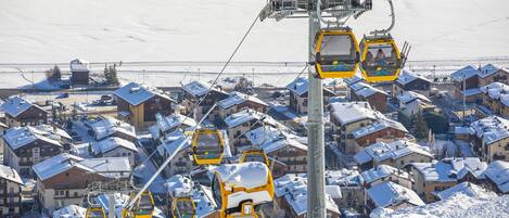 A ski lift with yellow cabins, a snow-covered village with buildings, and a clear sky.