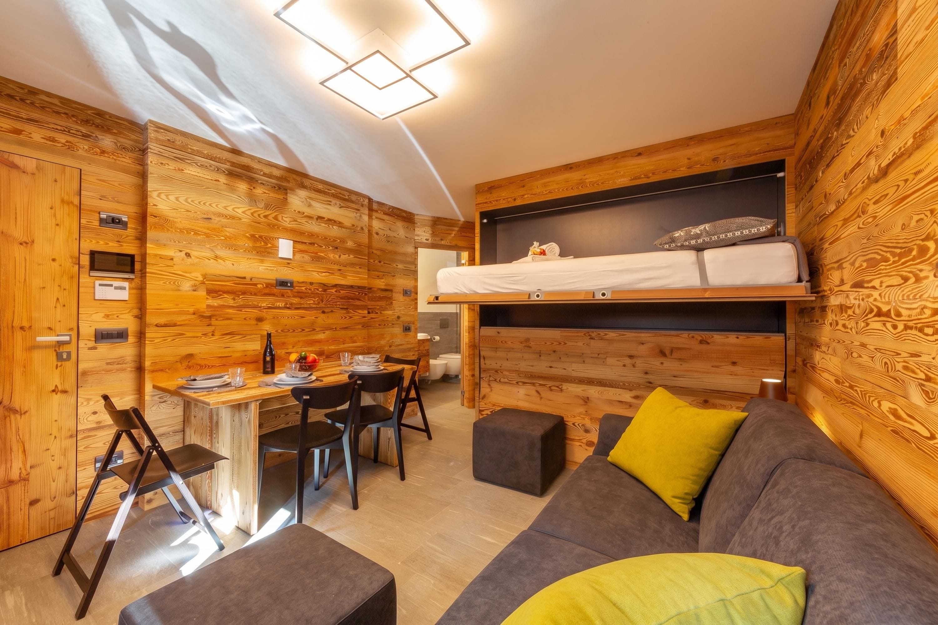 A compact room with a bunk bed, a dining table with chairs, a sofa, and a small kitchenette.