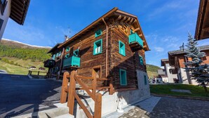 Une cabane en bois avec un escalier menant à un balcon, entourée d’une zone pavée et sous un ciel dégagé.