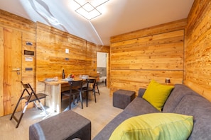 A modern interior with wooden panel walls, a dining area with a table and chairs, and a grey sofa with a yellow pillow. - Marlies Ski in - Ski out Mt.50 (Livigno)