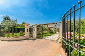 A gated entrance with a paved driveway leading to a building with a tiled roof.