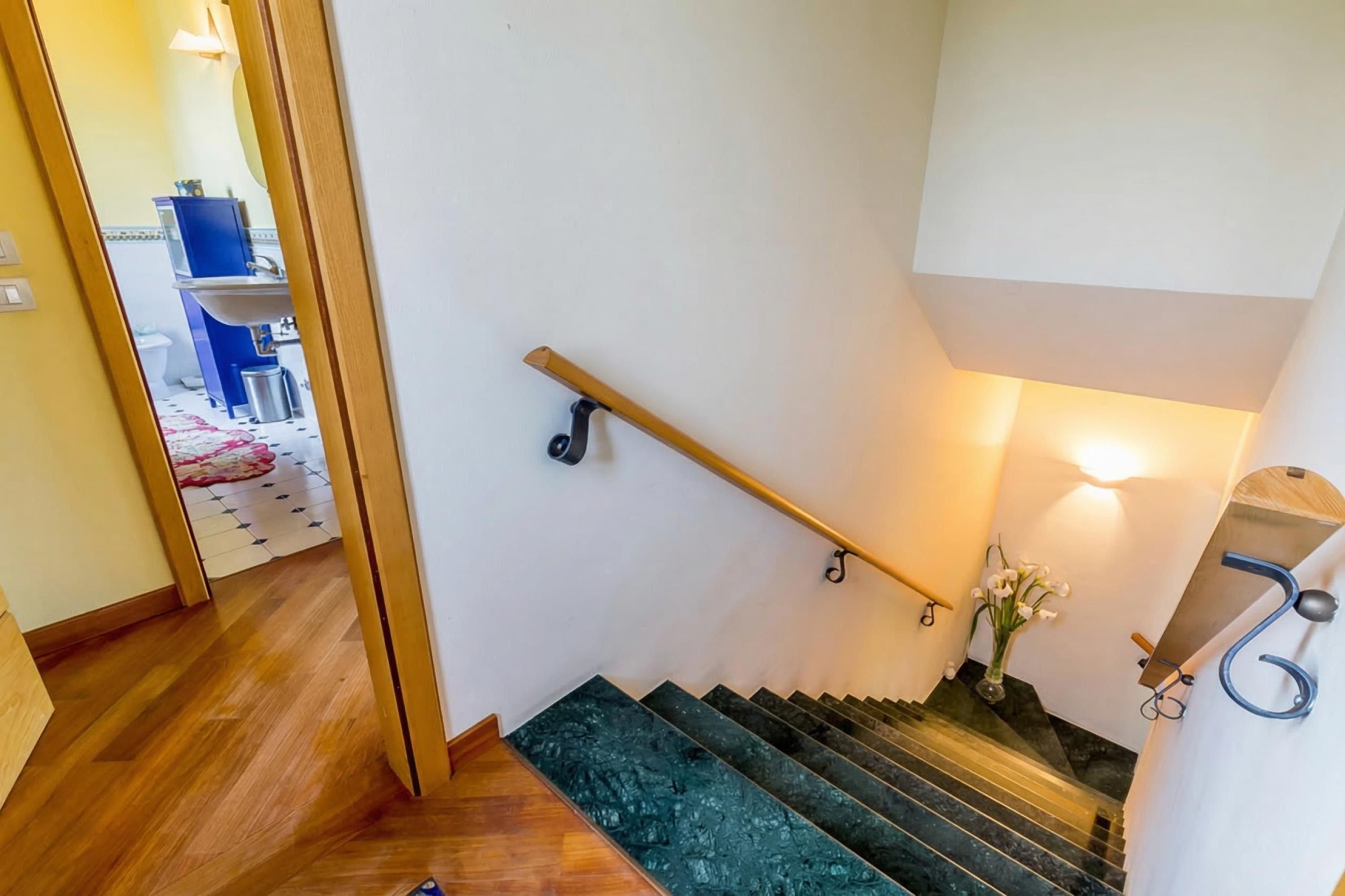 Eine Treppe mit hölzernem Geländer, einer Wandleuchte und einer kleinen Vase mit Blumen.