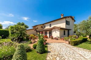 A two-story house with a stone pathway leading to the entrance, surrounded by well-maintained gardens and various flowering plants. - Villa Pallina With Pool (Massarosa)
