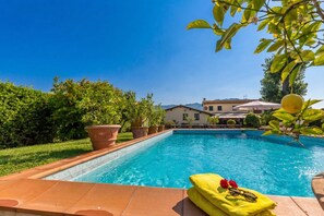 A swimming pool with a clear blue sky, surrounded by greenery and a building in the background. - Villa Pallina With Pool (Massarosa)