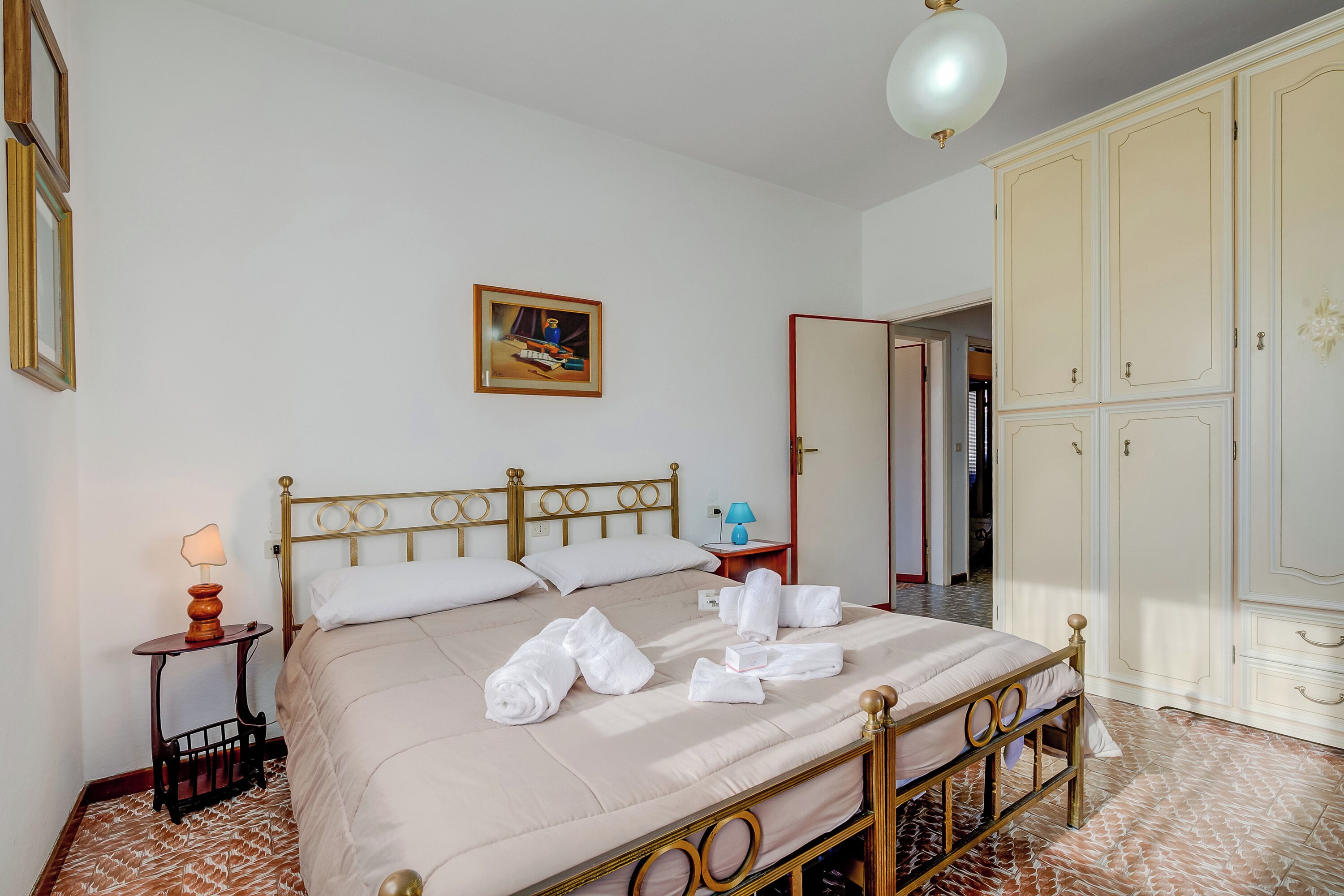 A neatly made bed with towels, a bedside table with a lamp, and a wardrobe.