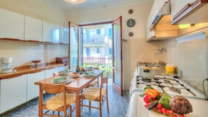 A kitchen with white cabinets, a stove, and a dining table with chairs. - Casa Vittoria 800m from sea (Forte dei Marmi)