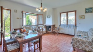 A dining area with a wooden table set for four, surrounded by chairs, a fireplace, and large windows. - Casa Vittoria 800m from sea (Forte dei Marmi)