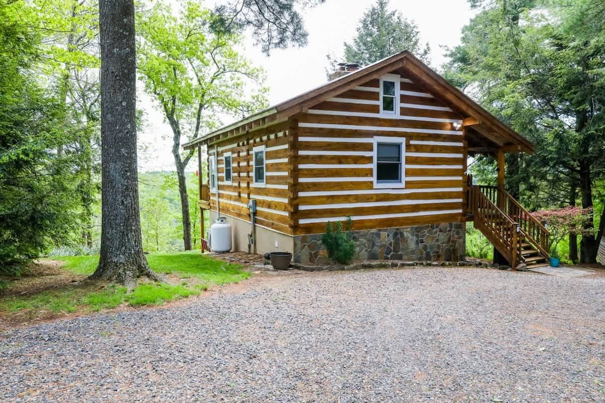 A log cabin with a stone foundation, a gravel driveway, and a wooden staircase leading to the entrance.