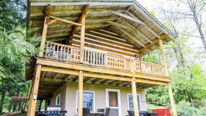 A two-story wooden cabin with a balcony, a grill outside, and a door with a window. - Touche' Too Cabin by Buffalo Mtn Getaway (Meadows of Dan)