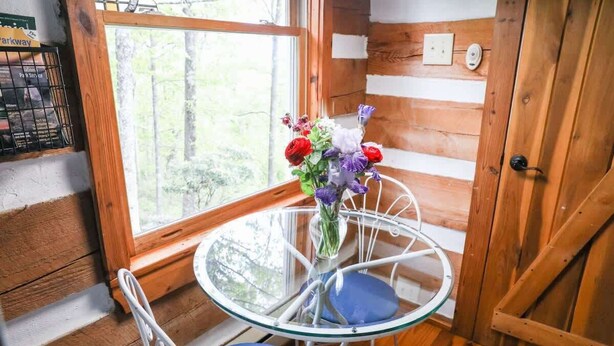 A wooden cabin interior with a glass table and chairs, a window with a view of trees, and a door with a rustic design. - Touche' Too Cabin by Buffalo Mtn Getaway (Meadows of Dan)