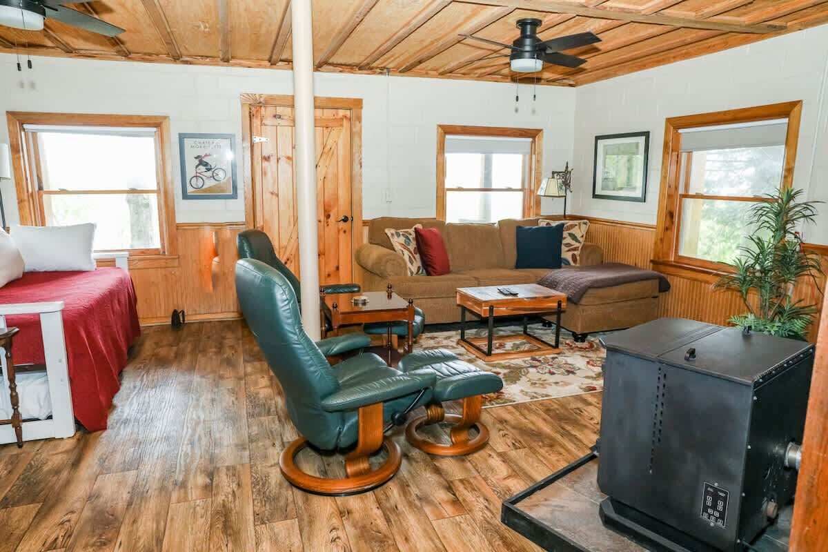 A cozy room with a wooden ceiling, a sofa, a chair, a table, a bed, and a fireplace.