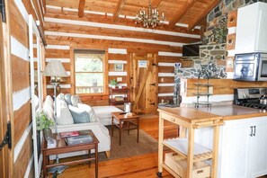 A cozy cabin interior with a wooden dining area, a sofa, and a kitchenette with a microwave and stove. - Touche' Too Cabin by Buffalo Mtn Getaway (Meadows of Dan)