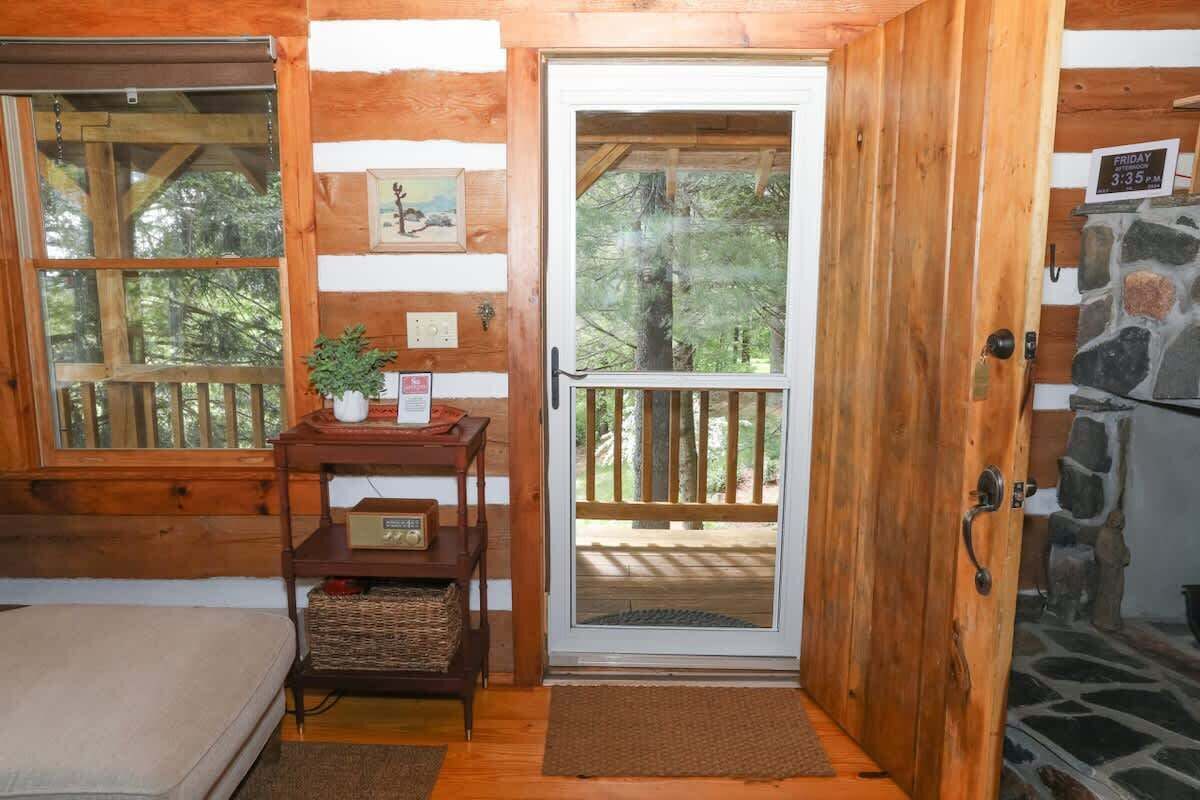 A wooden cabin interior with a door leading to a deck, a small table with a radio, and a bench.