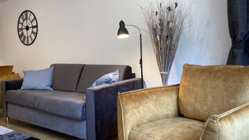 A living room with a grey sofa, a brown armchair, a floor lamp, and a wall clock.
