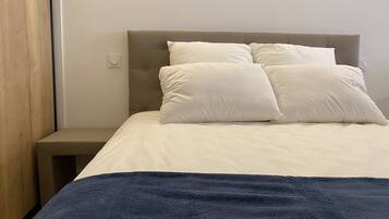 A bed with a headboard, two pillows, a bedside table, and a blue blanket.