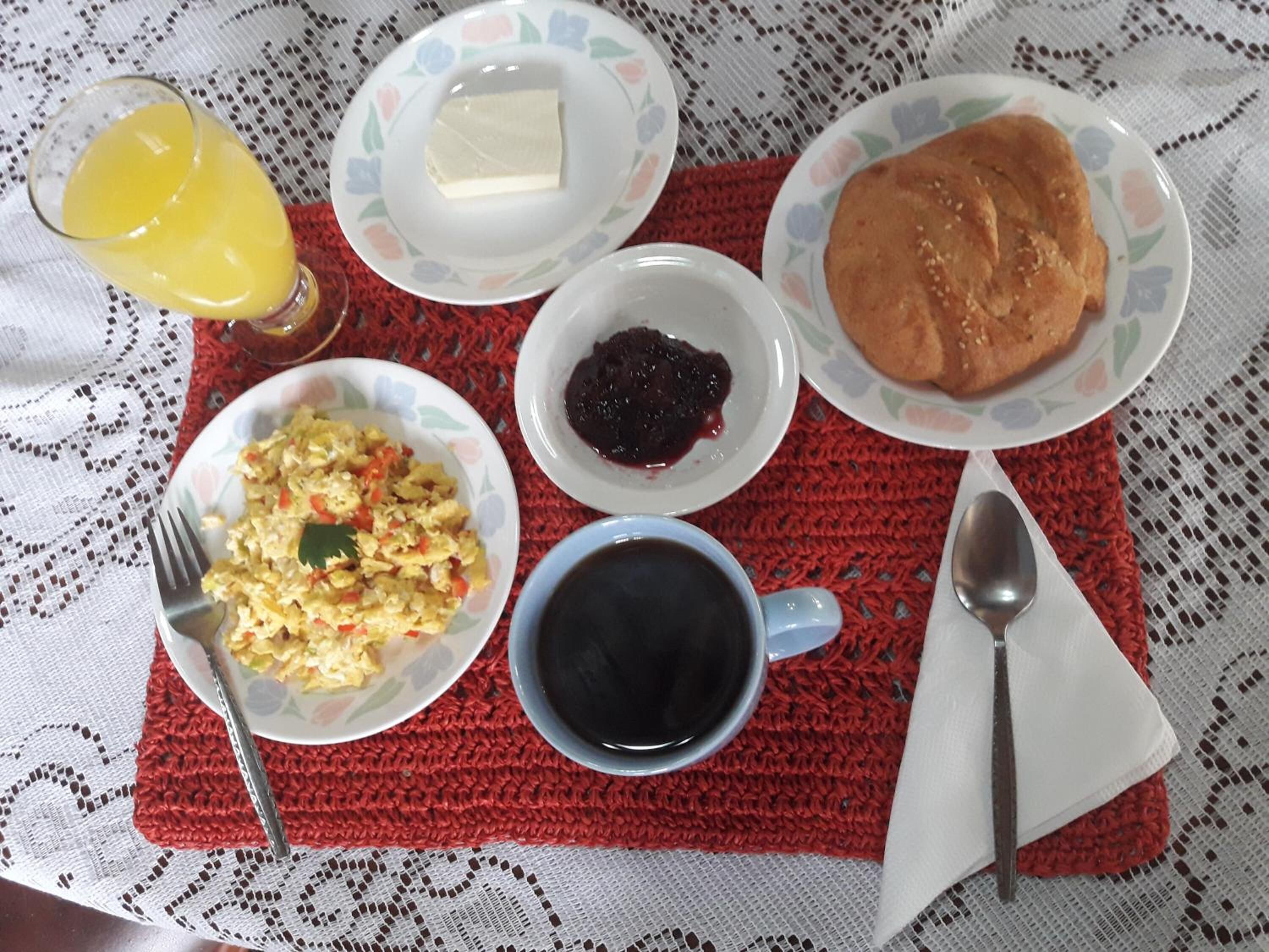 A breakfast table with scrambled eggs, butter, jam, pancakes, coffee, and a glass of orange juice.