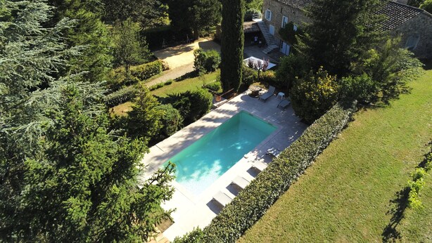 Una amplia piscina rectangular rodeada de césped cuidado y árboles, con un edificio de piedra al fondo.