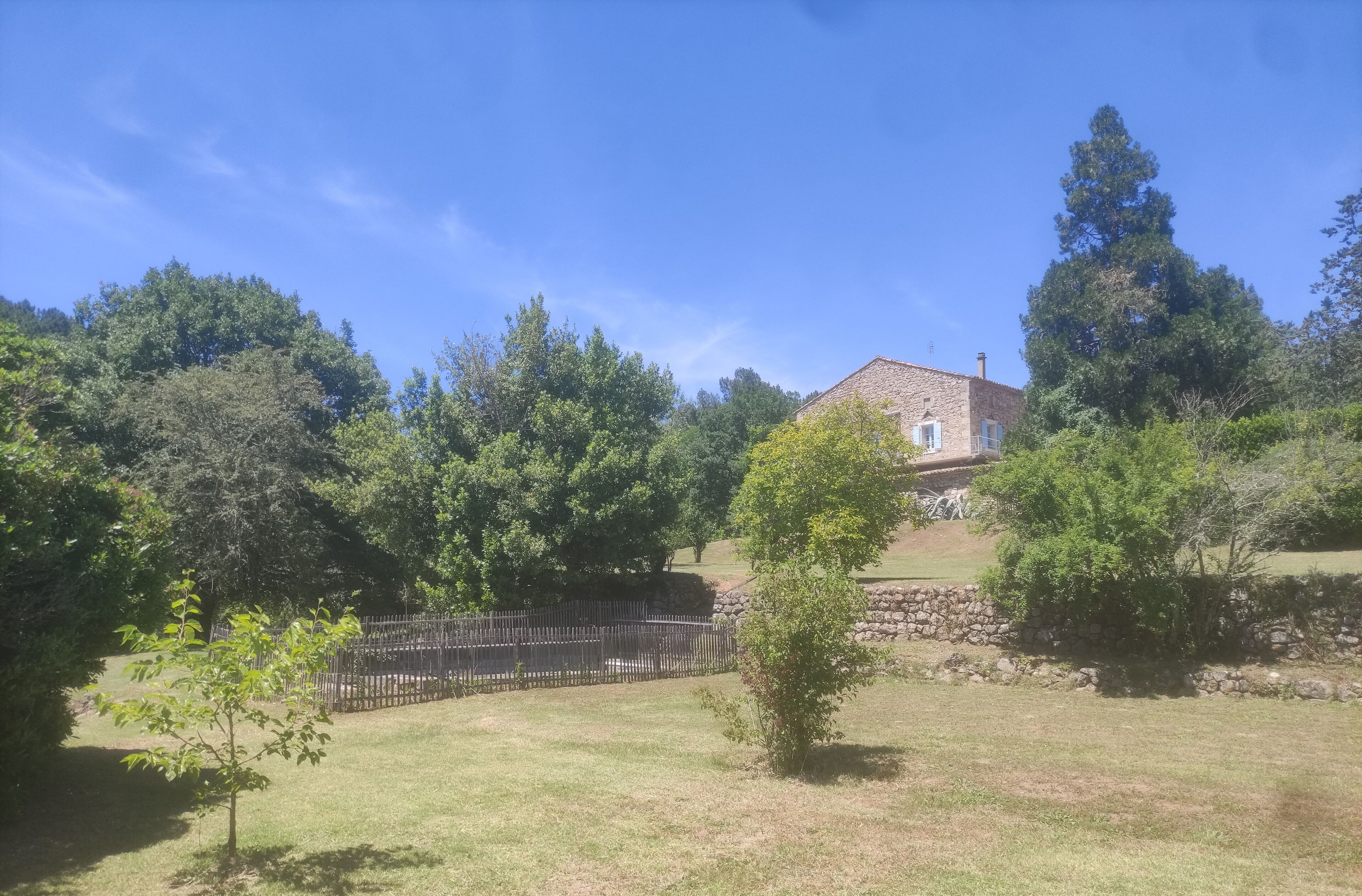 Una casa con un muro de piedra y un patio cercado, rodeada de árboles.