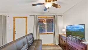 A room with a leather sofa, wooden dresser, ceiling fan, and a television displaying a scenic view.