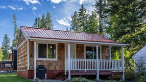 A wooden cabin with a porch, surrounded by trees.