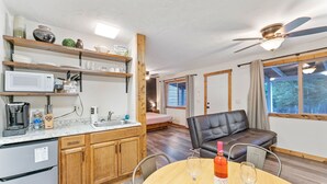 A compact living space with a kitchenette, a dining area with a table and chairs, a leather sofa, and a ceiling fan.