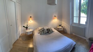 Une chambre à coucher avec un lit, deux tables de chevet, une plante en pot et un radiateur.