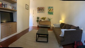 Un salon comprenant un canapé, une table basse, un téléviseur, une bibliothèque et une console sur laquelle sont disposés des objets décoratifs.