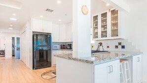 A modern kitchen with white cabinetry, a stainless steel refrigerator, a microwave, and a kettle on the countertop. - Panoramic Oceanfront Views from Beautiful Upper Level Home with Patio (Newport Beach)