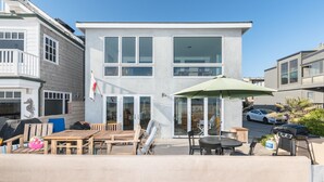 A modern two-story building with a patio area featuring outdoor furniture and a green umbrella. - Panoramic Oceanfront Views from Beautiful Upper Level Home with Patio (Newport Beach)