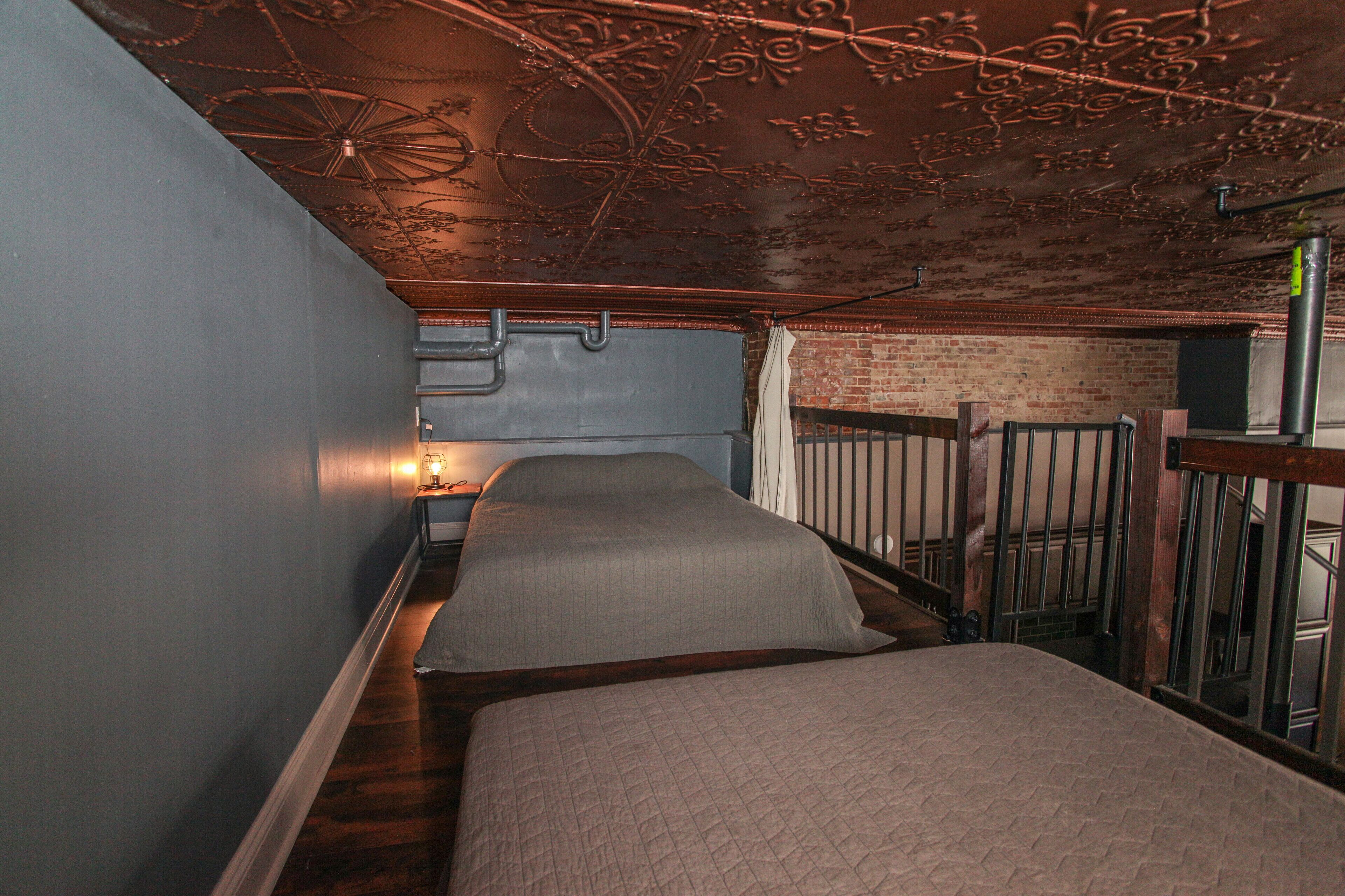 Ein schmaler Flur mit zwei Betten, einer Ziegelwand und einer Metalltreppe.