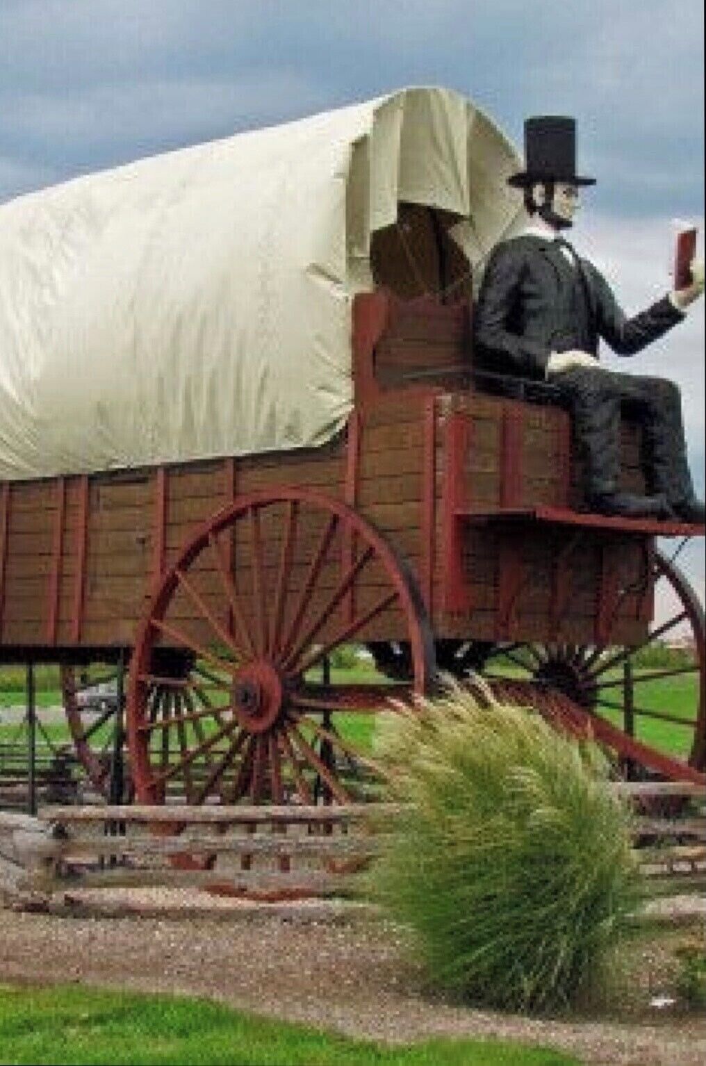 Un chariot couvert avec une silhouette assise à l’intérieur, entouré d’un champ verdoyant et d’une grande roue.