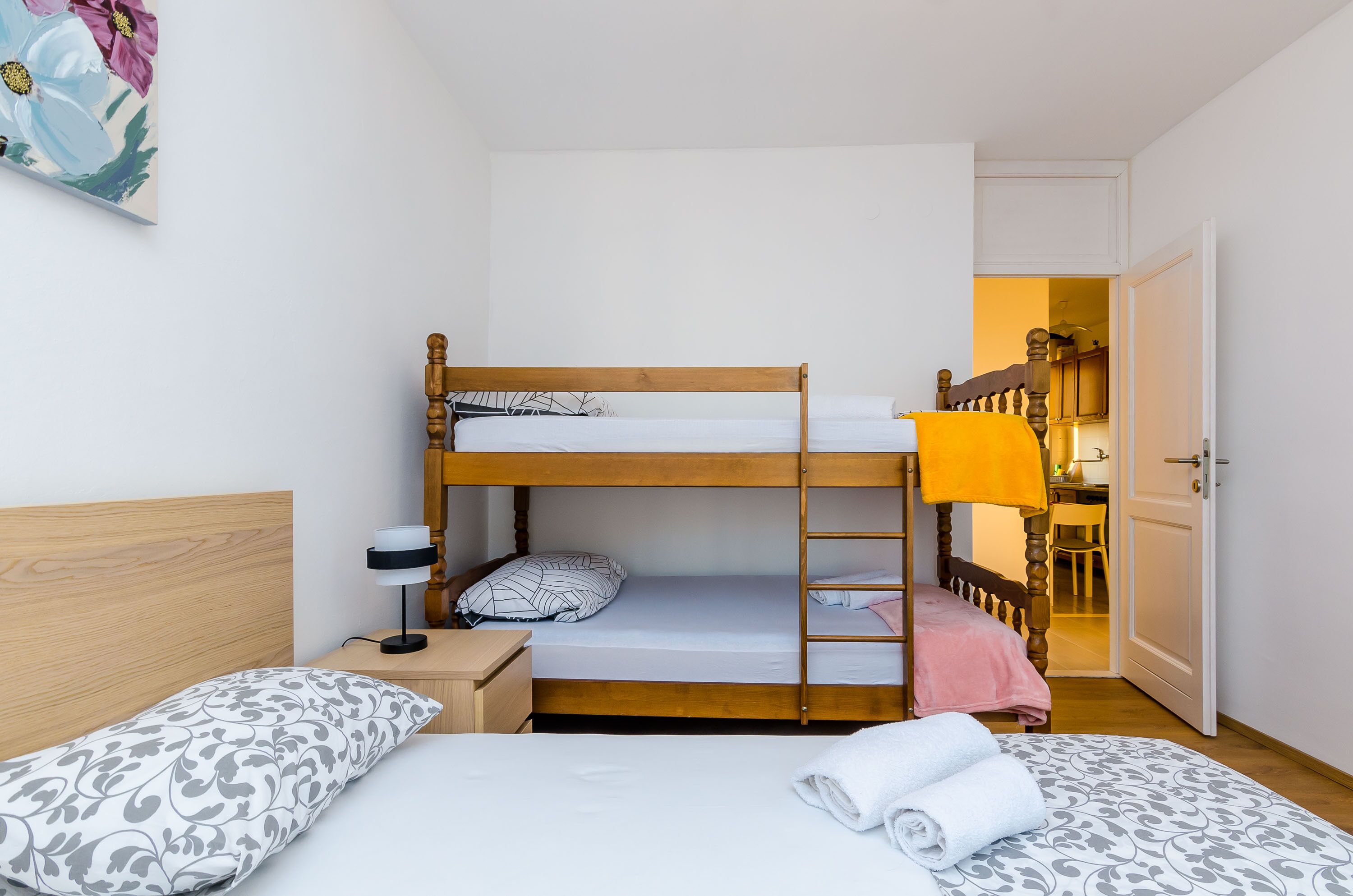 Habitación con literas, un escritorio, una silla y una puerta que da a otra habitación.