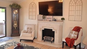 Una sala de estar con chimenea, un reloj y un televisor montado encima.