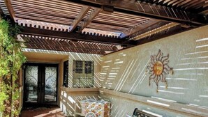 Un espacio al aire libre cubierto con un banco, una mesa con mantel estampado y una decoración de sol montada en la pared.