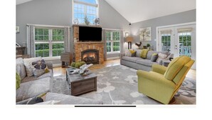 A spacious living room with a fireplace, comfortable seating, and large windows. - Beautiful Estate with salt water pool  & pond with kayaks  (Oak Bluffs)