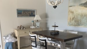 A dining area with a wooden table and four chairs, a chandelier, a lamp, and a painting on the wall.