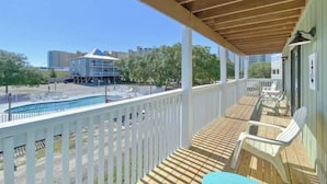 A covered outdoor area with a pool, wooden deck, and lounge chairs.