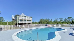 A swimming pool with a fenced deck, lounge chairs, and a building with a balcony in the background.
