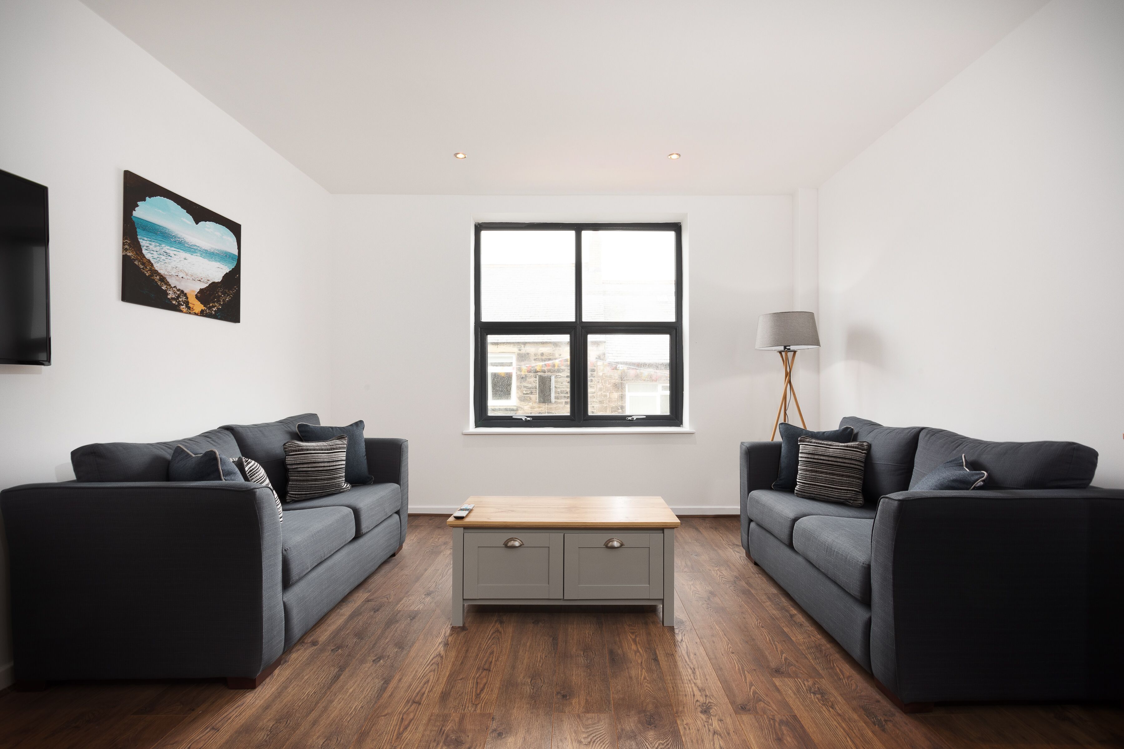 A modern living room with two dark sofas, a wooden coffee table, and a large window.
