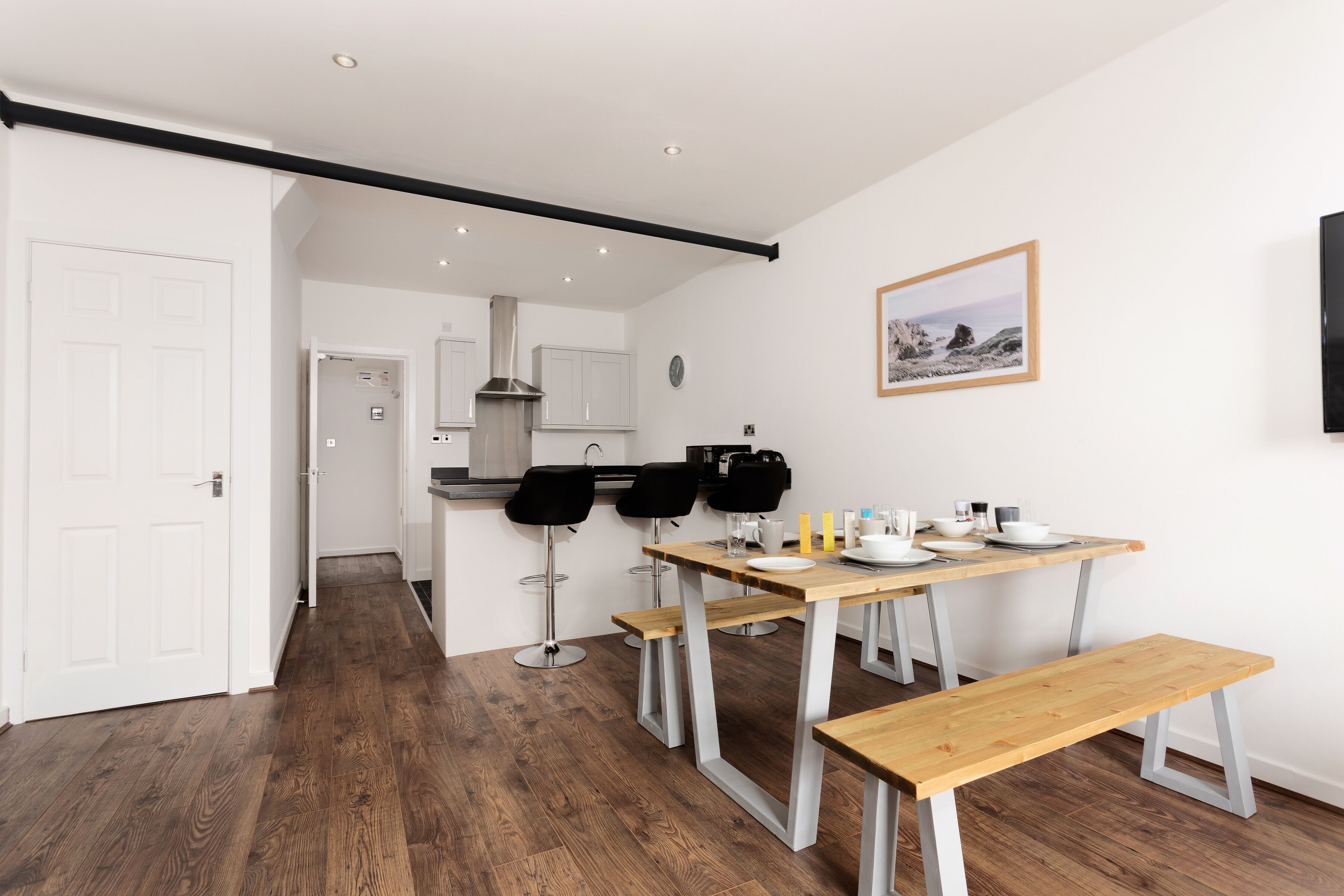 A modern kitchen with white cabinets, a stainless steel range hood, and a dining area with a wooden table and benches.