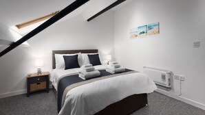 Een slaapkamer met een bed, nachtlampjes, een nachtkastje, een radiator en een plafondlamp.