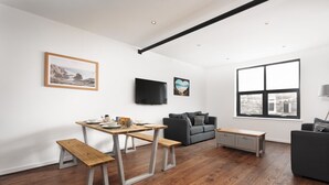 Een moderne woonkamer met een houten eettafel, bankjes, een grijze bank en een groot raam met uitzicht op de stad.