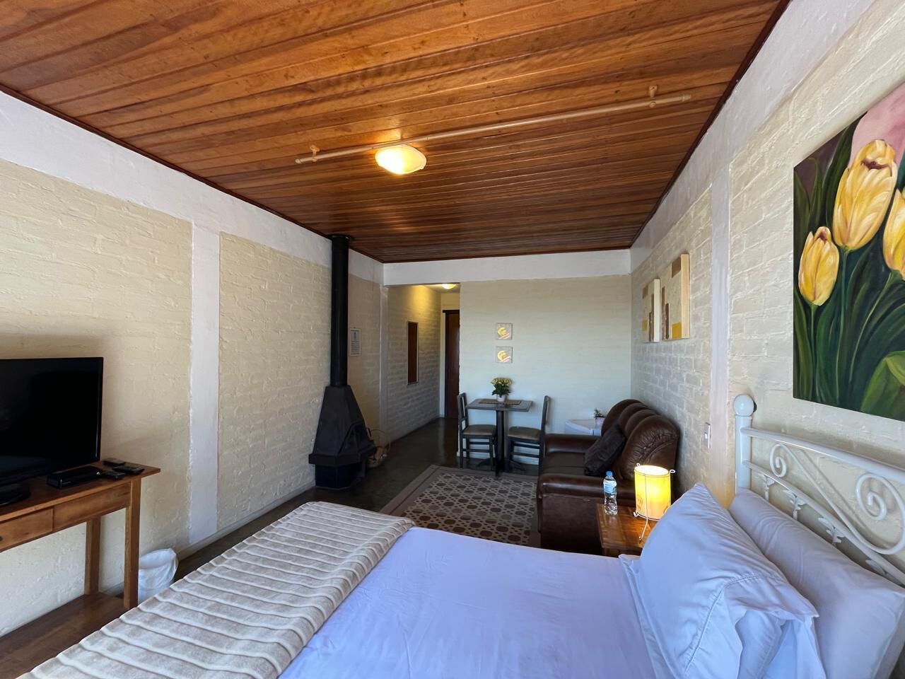 Un dormitorio con cama, televisión, chimenea, zona de comedor y un cuadro.