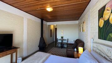 Un dormitorio con cama, televisión, chimenea, zona de comedor y un cuadro.